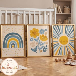 Peut inclure: Trois affiches encadrées représentant un arc-en-ciel bleu et jaune avec des points, un arrangement floral avec des fleurs jaunes et bleues, et un soleil souriant avec des rayons bleus et jaunes. Les cadres dorés reposent sur un sol en bois.