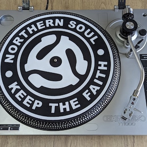 May include: Silver turntable with a black and white record featuring the text "NORTHERN SOUL KEEP THE FAITH". The turntable has a tonearm, volume controls, and the brand name "HOMEMIX TT1000".