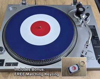 May include: A silver turntable with a blue, white, and red target design on the record. The turntable has a silver tone arm and a black power button. A matching target design keychain is included.