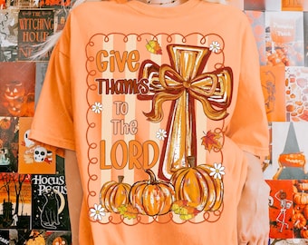 May include: Orange t-shirt with a fall-themed graphic. The design features a cross with a bow, pumpkins, and the text "Give Thanks To The Lord." Decorative leaves and flowers complete the design. The shirt is a comfortable, casual style.