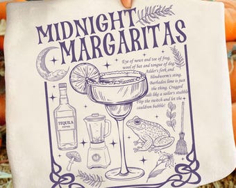 May include: A white tea towel featuring a purple illustration of a margarita cocktail, tequila bottle, blender, and a frog. The text "MIDNIGHT MARGARITAS" is at the top. The design includes a moon, a lime slice, and botanical elements.