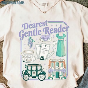 May include: Cream-colored t-shirt featuring a graphic design with the text "Dearest Gentle Reader." The design includes illustrations of a dress, carriage, teacup, and other elements in shades of purple, green, and white.