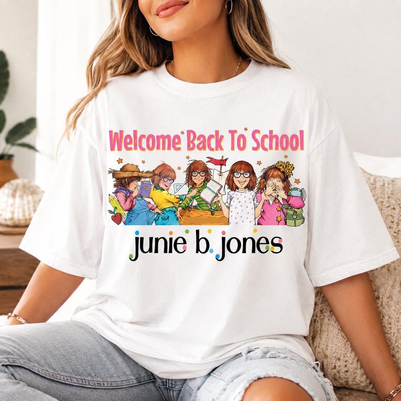 May include: A white short-sleeved t-shirt featuring a colorful graphic of five illustrated characters with the text Welcome Back To School and junie b. jones printed in black with multi-colored dots between the letters on the front of the shirt.