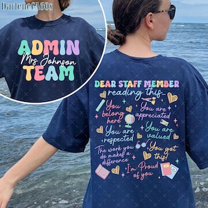 Puede incluir: Camiseta azul marino con las palabras "ADMIN TEAM" en letras de burbujas de colores. La parte posterior de la camiseta tiene el texto "DEAR STAFF MEMBER reading this..." con frases y gráficos de apoyo. Un regalo perfecto para profesores.