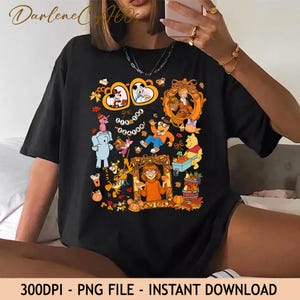 May include: A black short-sleeved t-shirt featuring a colorful graphic print of various cartoon characters, including Winnie the Pooh, Tigger, and Arthur, surrounded by autumn-themed elements like pumpkins, leaves, and the text 'Tis the Season'.