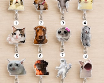 May include: A collection of twelve retractable badge reels featuring various cat and dog portraits, including memes and expressive animal faces. Each reel has a clear plastic housing and a numbered label from one to twelve for identification.