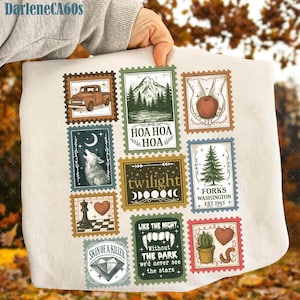 May include: A cream-colored blanket featuring a collage of postage stamp designs. The stamps depict various illustrations, including a truck, mountain scene, apple, wolf, chess piece, and cactus. Text includes "HOA HOA HOA", "twilight", and "FORKS WASHINGTON EST 1945".