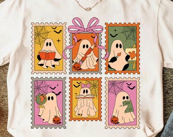 May include: White t-shirt featuring a colorful, retro-style design of six ghost illustrations within postage stamp frames. Each ghost is engaged in different activities, such as reading, drawing, and painting, with Halloween-themed elements like bats and pumpkins.