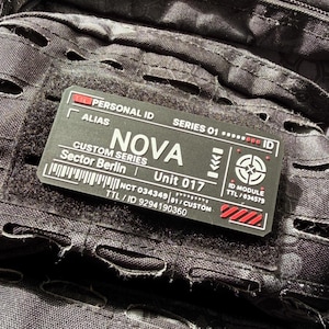 Puede incluir: Un parche táctico rectangular negro con texto blanco y detalles en rojo. El parche presenta el texto PERSONAL ID, ALIAS, SERIES 01, NOVA, CUSTOM SERIES, Sector Berlin, Unit 017, ID MODULE, TTL / 034579, NCT 034349 / 01 / CUSTOM, TTL / ID 9294190360.