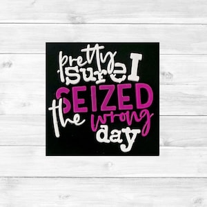 May include: A black square with the phrase "pretty sure I seized the wrong day" in white and magenta lettering. The words are in a whimsical, handwritten style, set against a white wooden background.