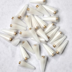 May include: A pile of white plastic cone-shaped tips with a gold metal base. The tips are used for a variety of applications, including crafts, hobbies, and DIY projects.