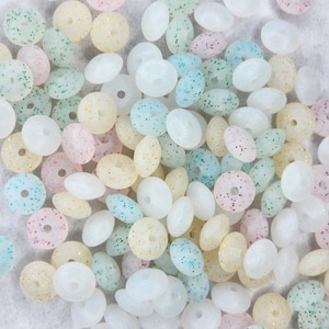 May include: A collection of pastel-colored donut-shaped beads with glitter embedded in the plastic. The beads are in shades of pink, blue, green, and yellow.