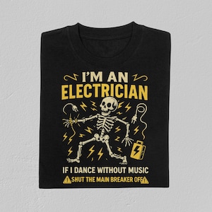 Puede incluir: Camiseta negra con un gráfico amarillo de un esqueleto sosteniendo cables eléctricos y una caja de herramientas. El texto dice "I'M AN ELECTRICIAN" y "IF I DANCE WITHOUT MUSIC SHUT THE MAIN BREAKER OFF".