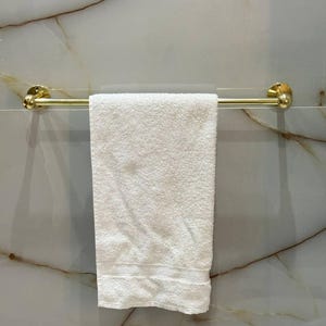 Close-up of round escutcheon and straight bar in unlacquered brass; hand-polished surface shows natural grain. Solid brass hardware resists corrosion and adds heirloom character to powder rooms and primary baths.