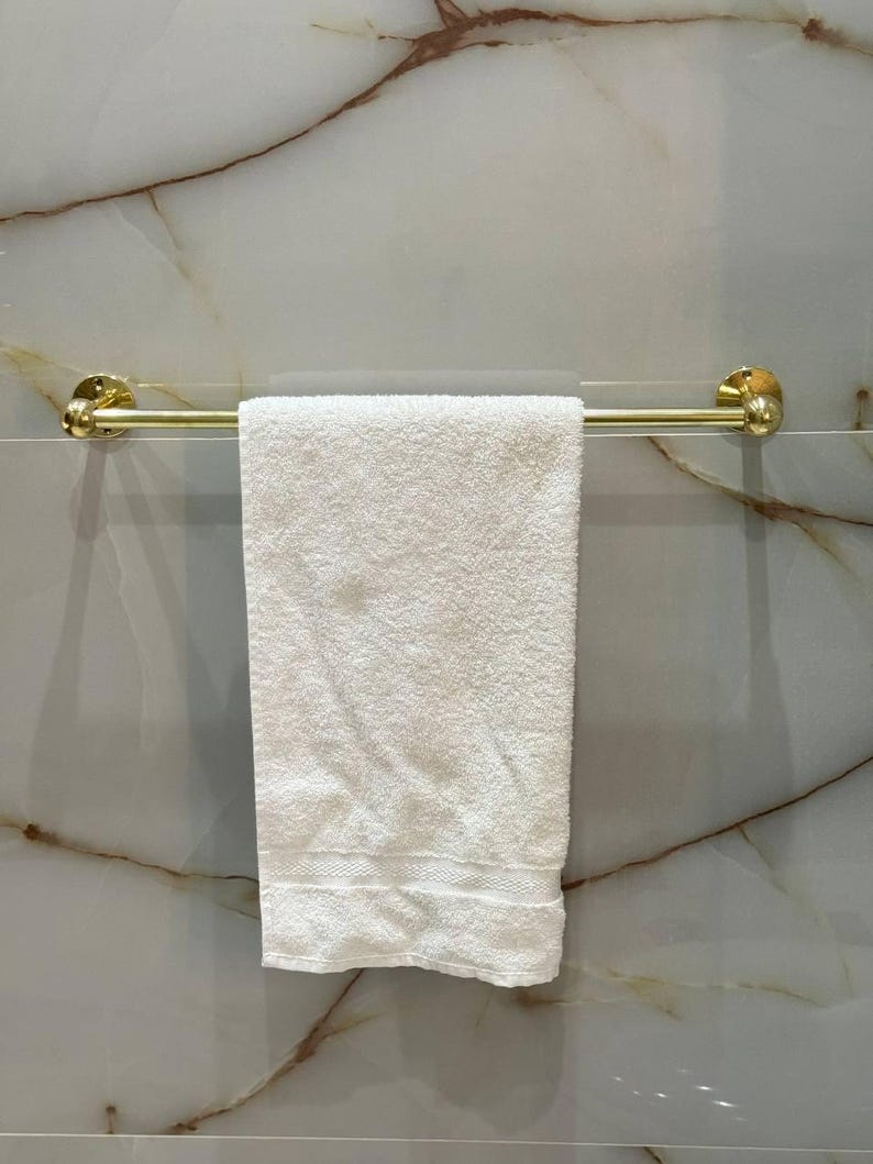 Close-up of round escutcheon and straight bar in unlacquered brass; hand-polished surface shows natural grain. Solid brass hardware resists corrosion and adds heirloom character to powder rooms and primary baths.