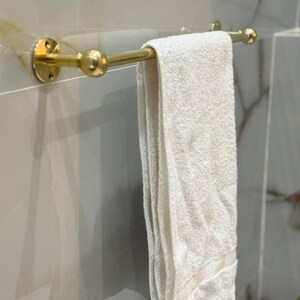 Styled vignette: warm raw brass towel bar against stone tile with folded linens and greenery. Perfect upgrade for guest bath, Airbnb, or modern farmhouse interiors; mixes well with marble and wood accents.