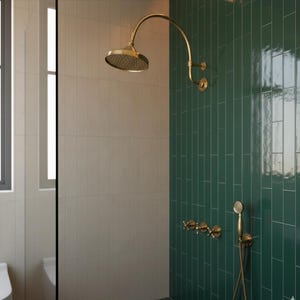 May include: A gold-colored shower head and fixtures are mounted on a dark green tiled wall. The shower head has a curved arm. The wall is tiled in a vertical brick pattern. The adjacent wall is tiled in a light beige color.