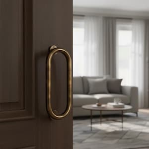 Könnte beinhalten: Nahaufnahme einer dunkelbraunen Holztür mit einem goldfarbenen, ovalen Türgriff. Die Tür ist leicht geöffnet und gibt den Blick auf ein Wohnzimmer mit grauem Sofa, rundem Couchtisch und gemustertem Teppich frei.