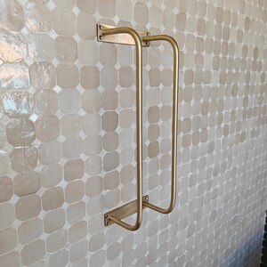DIY installation shot: raw brass towel organizer with mounting screws and wall anchors; 24″ wide bar fits standard studs; unlacquered finish arrives hand-polished and will darken over time to a honey-bronze patina; ships from USA.