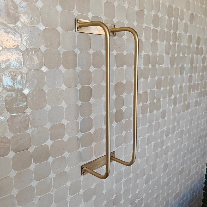DIY installation shot: raw brass towel organizer with mounting screws and wall anchors; 24″ wide bar fits standard studs; unlacquered finish arrives hand-polished and will darken over time to a honey-bronze patina; ships from USA.
