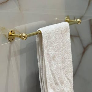 Bathroom scene with multiple unlacquered brass towel bars for layered storage of hand towels and bath sheets. Living-finish brass develops natural patina over time; ideal for French-country, rustic, or coastal bathrooms.