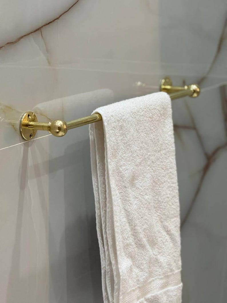 Bathroom scene with multiple unlacquered brass towel bars for layered storage of hand towels and bath sheets. Living-finish brass develops natural patina over time; ideal for French-country, rustic, or coastal bathrooms.