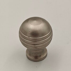 Puede incluir: Un pomo de metal plateado con un dise&ntilde;o redondo y estriado. El pomo tiene un acabado liso y pulido.