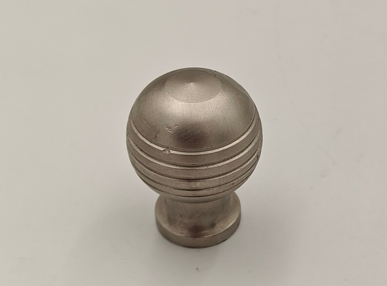 Puede incluir: Un pomo de metal plateado con un dise&ntilde;o redondo y estriado. El pomo tiene un acabado liso y pulido.