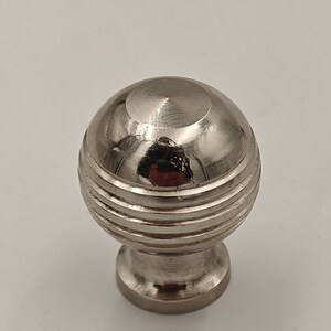 Puede incluir: Un pomo redondo de armario plateado con un dise&ntilde;o acanalado.