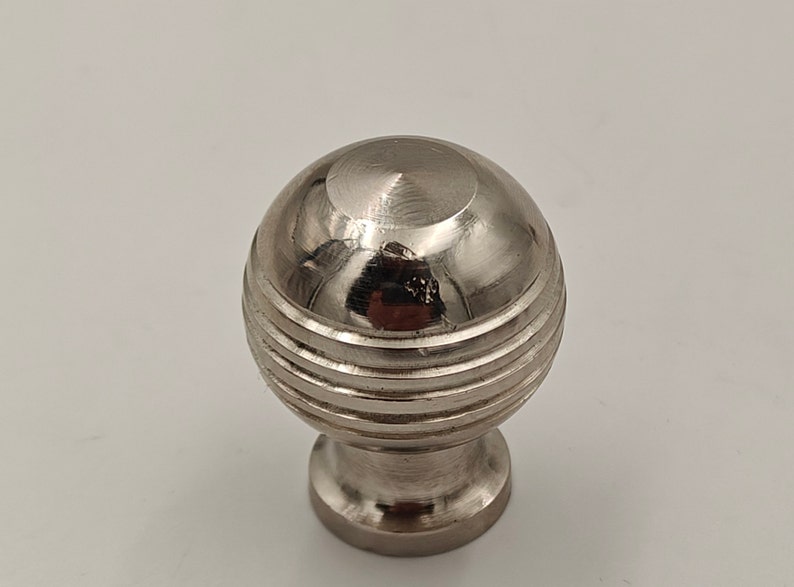 Puede incluir: Un pomo redondo de armario plateado con un dise&ntilde;o acanalado.