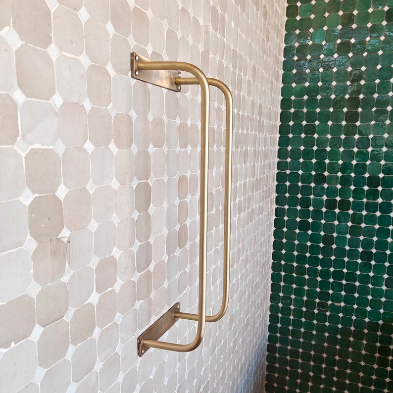 Styled vignette: a folded linen towel draped over the unlacquered brass towel rack above a marble countertop vanity; warm golden tones of raw brass complement wood accents, greenery, and antique hardware; ideal for bathroom towel storage and décor.