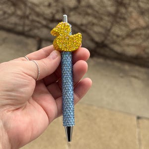 Könnte beinhalten: Ein blauer und gelber Strass-Stift mit einer gelben Gummiente auf der Oberseite.