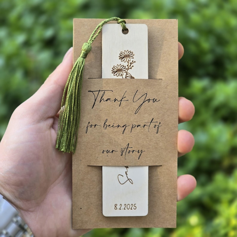 Pode incluir: Um cart&atilde;o castanho com um marcador de p&aacute;gina de madeira anexado. O marcador de p&aacute;gina tem um design floral e o texto "Thank You for being part of our story" e "8.2.2025".