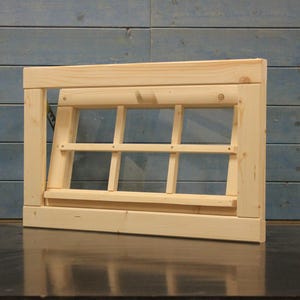 Könnte beinhalten: Ein Holzfensterrahmen mit einem Gitter aus neun Fensterscheiben. Das Fenster ist geöffnet und der Rahmen ist aus unbehandeltem Holz.