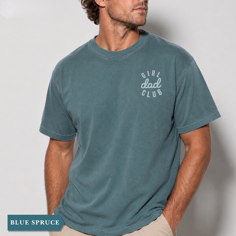 Puede incluir: Camiseta de color azul abeto con el texto "GIRL dad CLUB" en un dise&ntilde;o blanco y circular en la parte superior del pecho. La camiseta tiene mangas cortas y cuello redondo. La parte inferior de la imagen tiene el texto "BLUE SPRUCE".