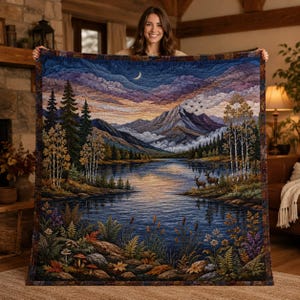 May include: A rectangular quilt featuring a detailed landscape scene of a lake surrounded by pine trees, birch trees, and mountains under a twilight sky with a crescent moon. Two deer stand on the shore near colourful wildflowers and ferns.