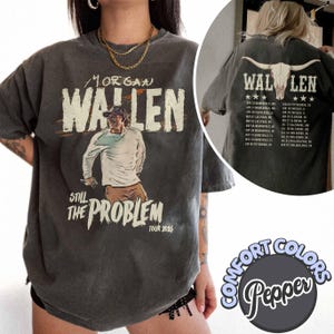 Puede incluir: Camiseta gris oscuro con un gráfico de Morgan Wallen y el texto "Still The Problem Tour 2026". La parte posterior de la camiseta muestra una calavera de toro y las fechas de la gira. La camiseta es de Comfort Colors.
