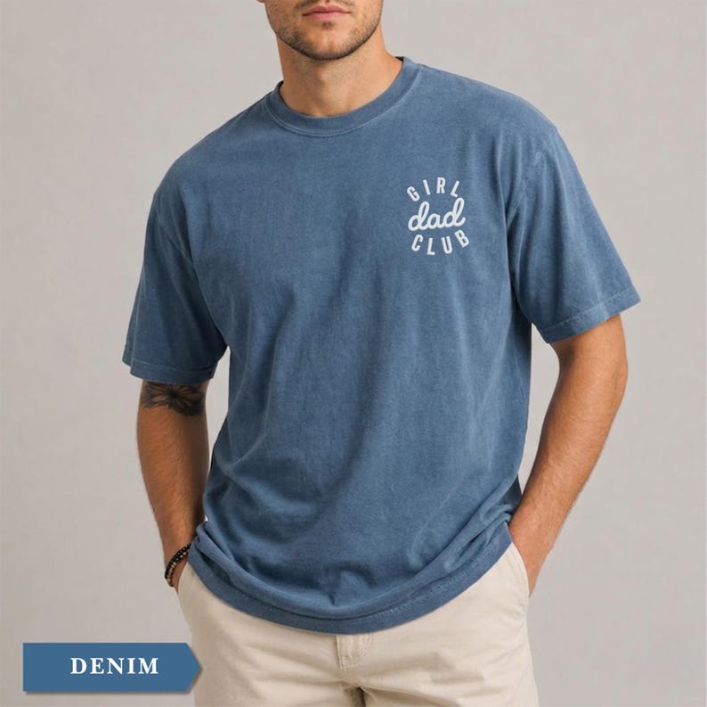 Puede incluir: Camiseta azul denim con el texto "GIRL dad CLUB" en blanco en la parte superior de la espalda. La camiseta tiene cuello redondo y mangas cortas. El modelo lleva pantalones color caqui. La palabra "DENIM" est&aacute; en un rect&aacute;ngulo azul en la parte inferior.