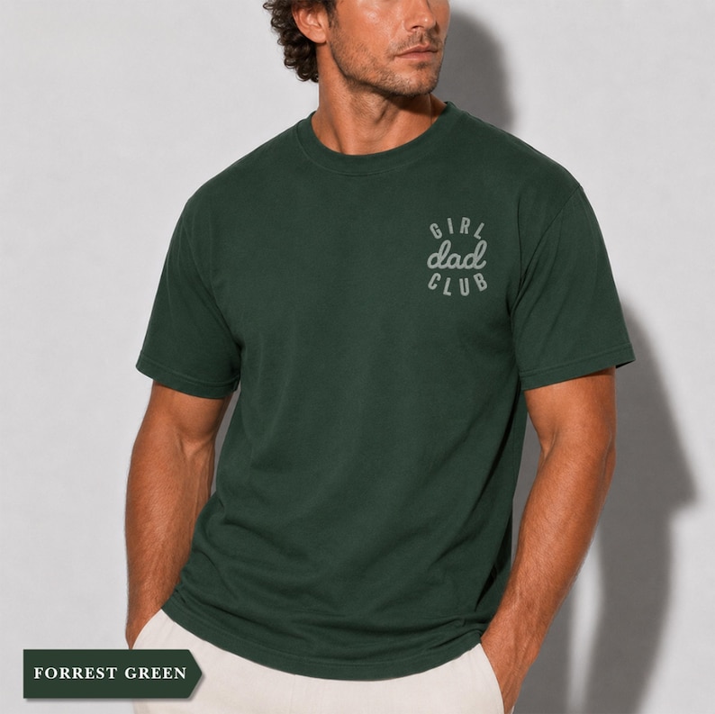 Puede incluir: Camiseta verde bosque con el texto "Girl Dad Club" en escritura gris claro en el pecho. La camiseta es de color liso y tiene un dise&ntilde;o cl&aacute;sico de cuello redondo. Las palabras "Forrest Green" se muestran en un recuadro en la parte inferior.