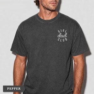 Puede incluir: Camiseta gris oscuro de manga corta con el texto "GIRL dad CLUB" en una fuente estilizada en la parte superior del pecho. La camiseta tiene un aspecto vintage y desgastado. La palabra "PEPPER" se muestra en un recuadro en la parte inferior.