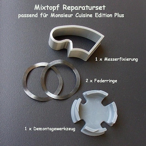 Könnte beinhalten: Ein Satz Ersatzteile für einen Monsieur Cuisine Edition Plus Küchenroboter. Das Set enthält ein graues Kunststoffwerkzeug, zwei Metallringe und einen Metallmesserhalter. Die Teile liegen auf einer grauen Oberfläche.