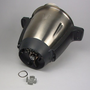 Könnte beinhalten: Ein zerlegter silberner Küchenroboter mit schwarzem Sockel. Der Sockel hat eine kreisförmige Öffnung mit einem sichtbaren Metallgetriebe. Ein silberner Ring und ein graues Kunststoffteil liegen auf einer weißen Oberfläche.