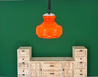May include: A set of three wooden cabinets with drawers, featuring a carved design. The cabinets are arranged in a row, with a bright orange pendant light hanging above them against a green wall.