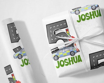 May include: White wrapping paper with a repeating pattern of a police car, a traffic light, a stop sign, and a traffic cone. The paper also has a gray road with white dashed lines and the name "Joshua" in green letters.