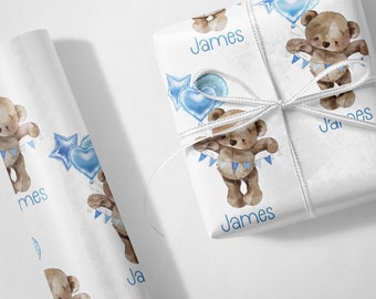 May include: White wrapping paper with a blue and white teddy bear design. The paper has the name "James" printed on it.