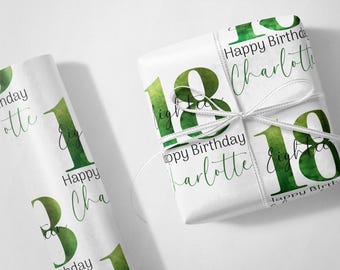 May include: White gift wrap with a green watercolor "18" and "Happy Birthday Charlotte" text. A wrapped gift is tied with a white ribbon. A roll of matching wrapping paper is visible.