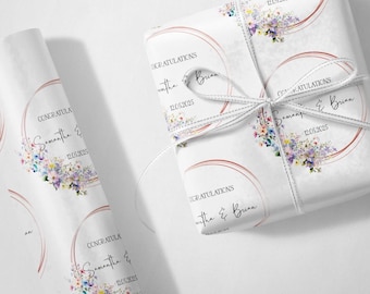 May include: White gift wrap with a floral design and the text "CONGRATULATIONS Samantha & Brian 12.05.2025". The wrap is tied with a white ribbon. A roll of the same wrapping paper is also visible.