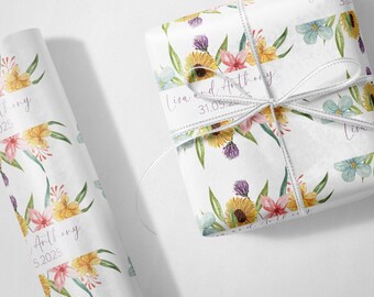 May include: White floral gift wrap with a watercolor design featuring sunflowers, pink and yellow flowers, and green leaves. The wrapped gift is tied with a white ribbon. The text "Lisa and Anthony 31.05.2025" is printed on the wrap.