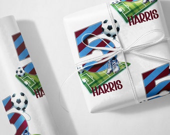 May include: White wrapping paper with a repeated pattern of a soccer ball, a number 5, a soccer field, and the name "HARRIS". The number 5 is in blue and maroon stripes. The soccer field is green with white lines. The soccer ball is black and white. The name "HARRIS" is in black.