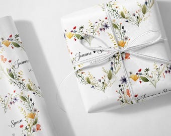 May include: White gift wrap with a floral design featuring yellow, red, and purple flowers. The wrapped gift is tied with a white ribbon. The text "Joanne" and "Simon" are printed on the wrap.